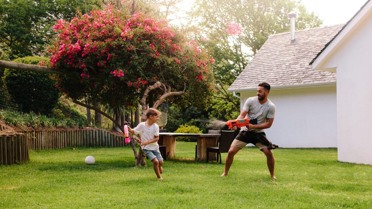 A father and son playing with water guns on a back lawn
