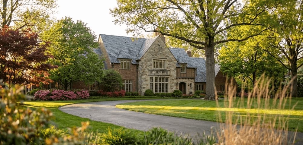 A large stone house set back from a curving drive among mature trees